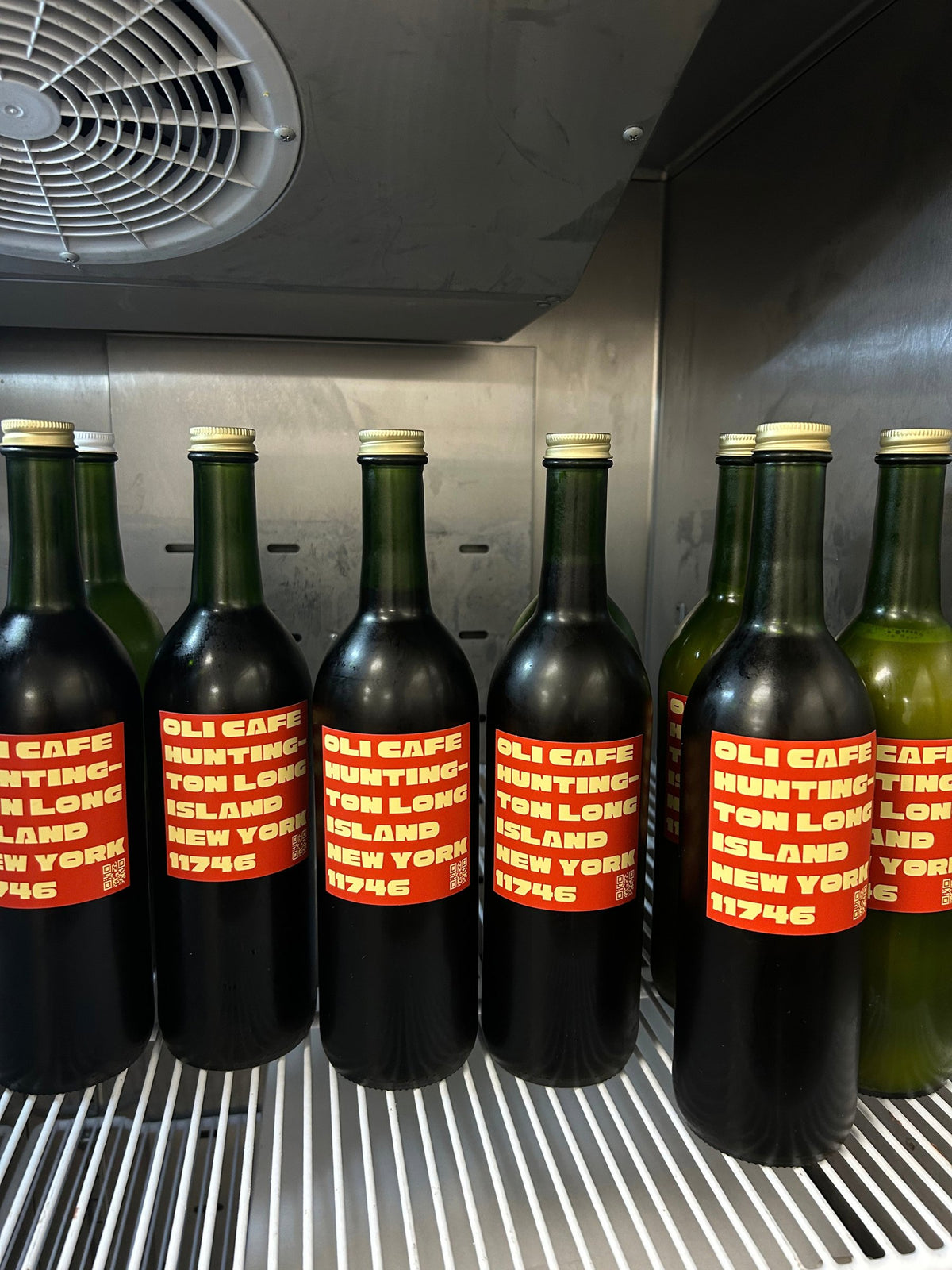 OLI CAFÉ bottles with red labels lined up in a fridge